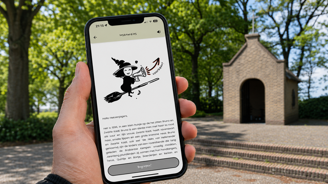 Hand houdt een smartphone vast met de instructies van Heksenjacht Bladel op het scherm, met op de achtergrond het kapelletje in Bladel.